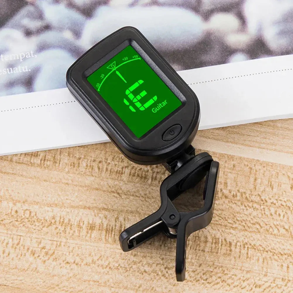 Digital clip-on guitar tuner with green display, shown on a wooden surface