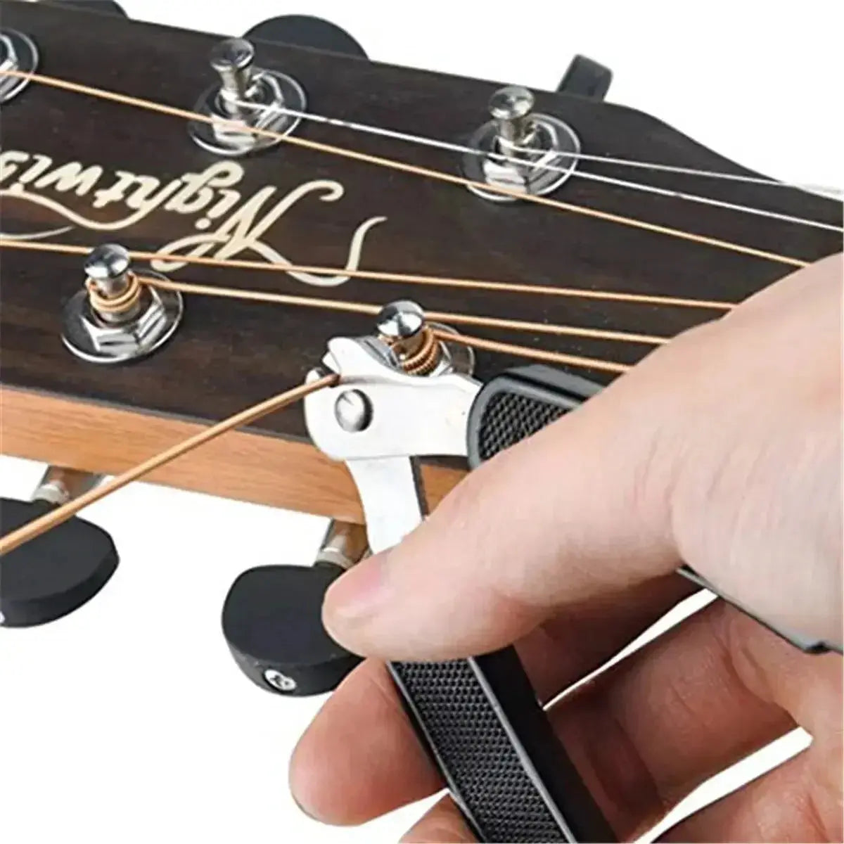 Hand using a 3-in-1 guitar string winder and cutter tool on an acoustic guitar headstock
