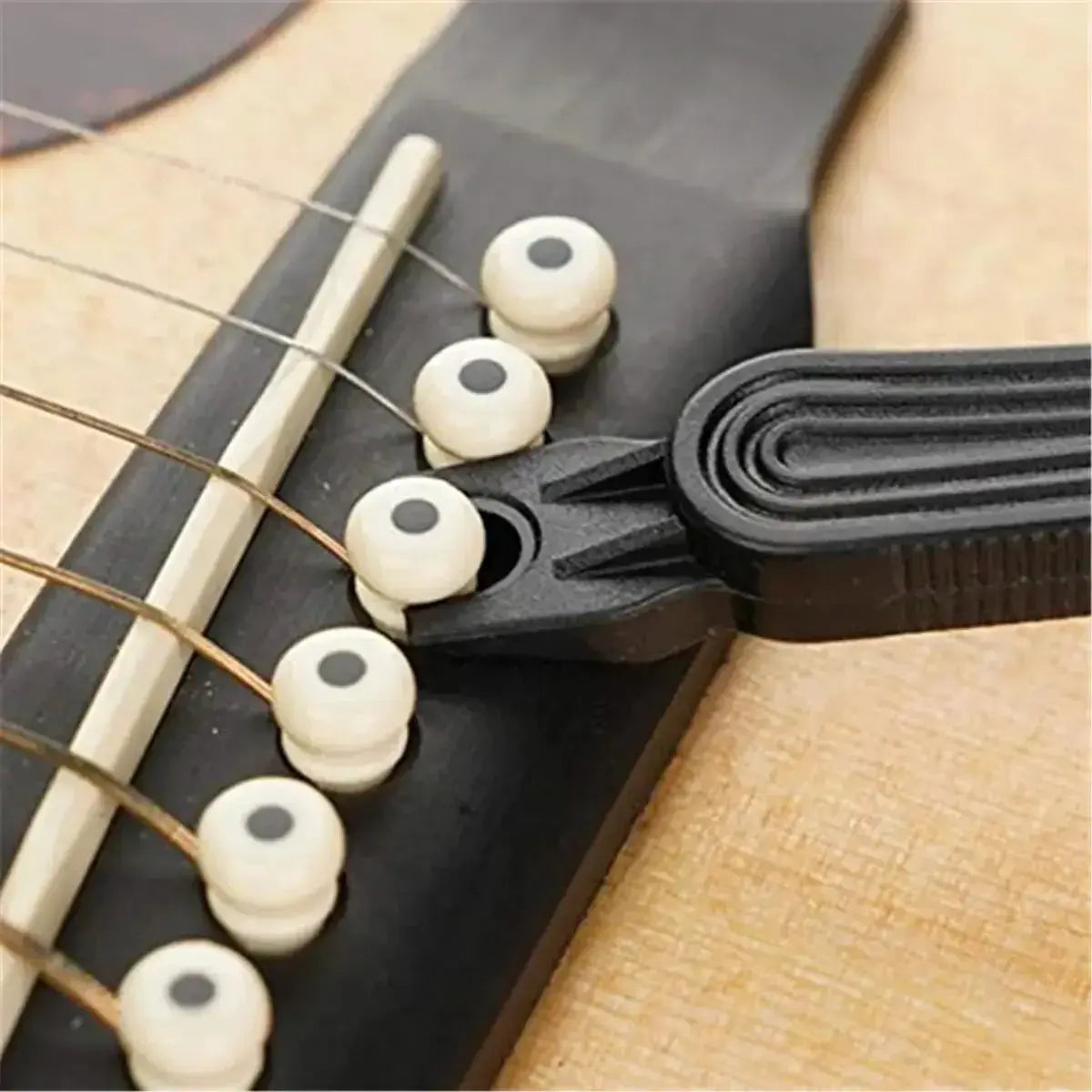 Guitar string winder tool removing bridge pin from acoustic guitar bridge.