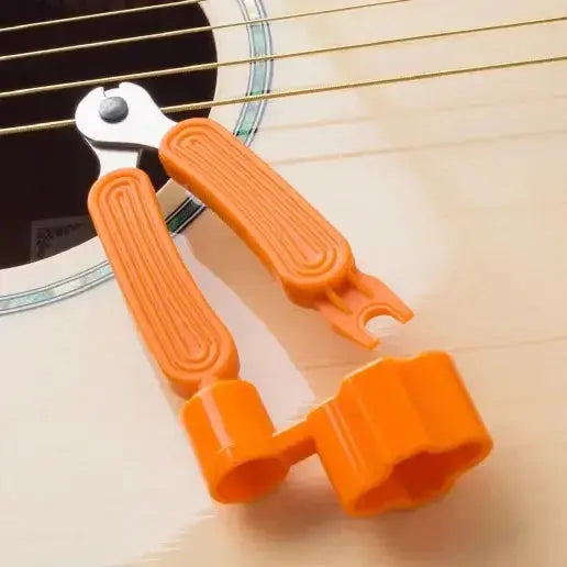 Orange 3-in-1 guitar string winder, cutter, and bridge pin puller tool on acoustic guitar